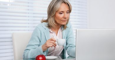 mujer adulta mayor sentada tomando una taza de café frente a un monitor de computadora