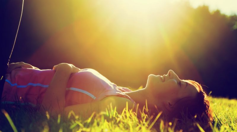 Mujer recostada en el pasto con los ojos cerrados tomando un poco de sol