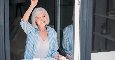 mujer adulta mayor asomada en la ventana con un periódico en la mano y una taza de café